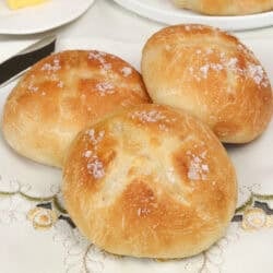 a small batch of french bread dinner rolls on a tablecloth next to a stick of butter.