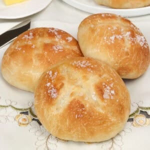 a small batch of french bread dinner rolls on a tablecloth next to a stick of butter.
