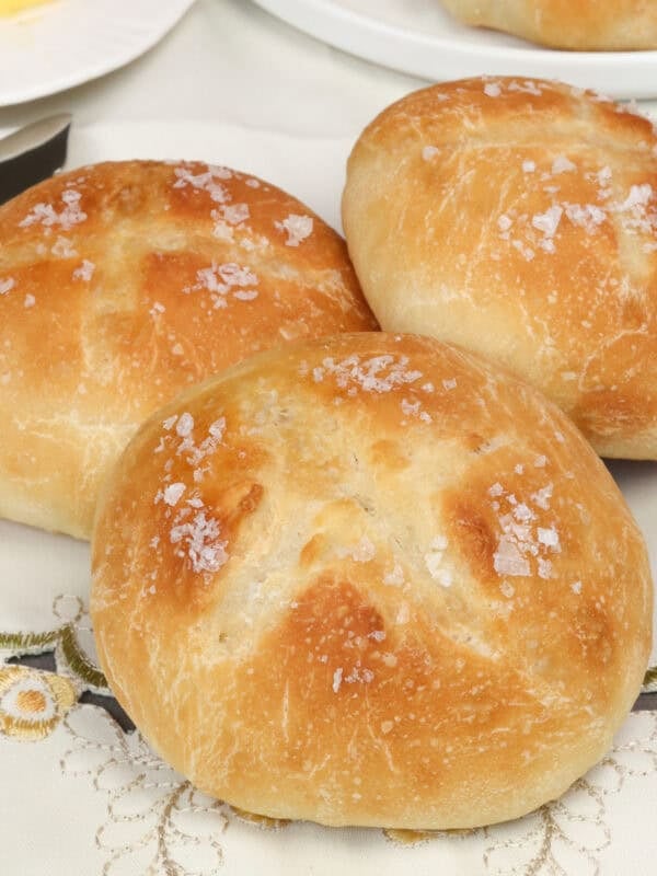 a small batch of french bread dinner rolls on a tablecloth next to a stick of butter.