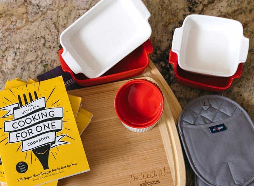 collection of square and rectangle single serving baking dishes with a cooking for one cookbook and oven mitt.