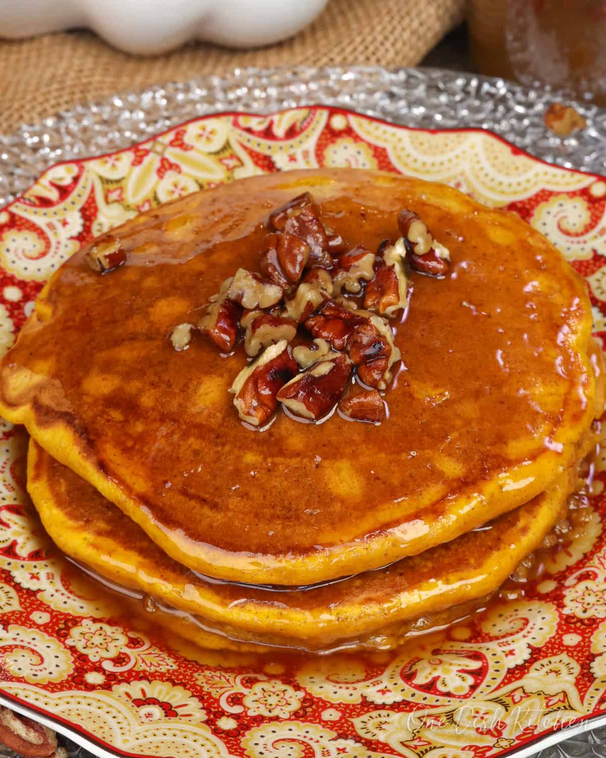 a small batch of fluffy pumpkin pancakes for one person on a plate topped with syrup and pecans.