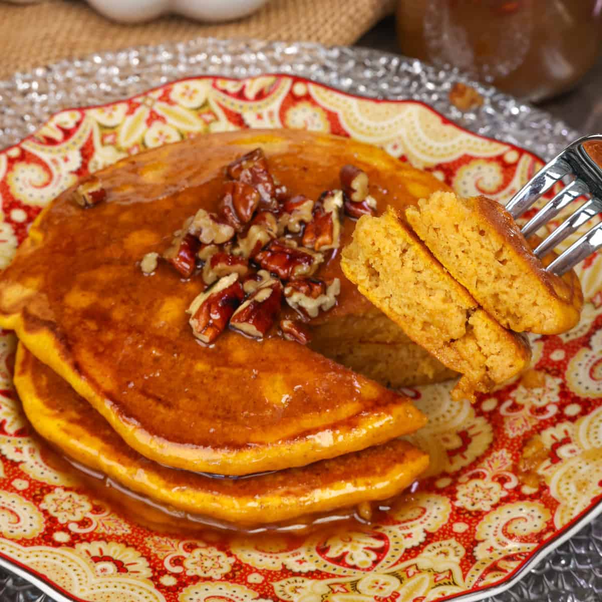 a small batch of fluffy pumpkin pancakes topped with syrup on a plate.