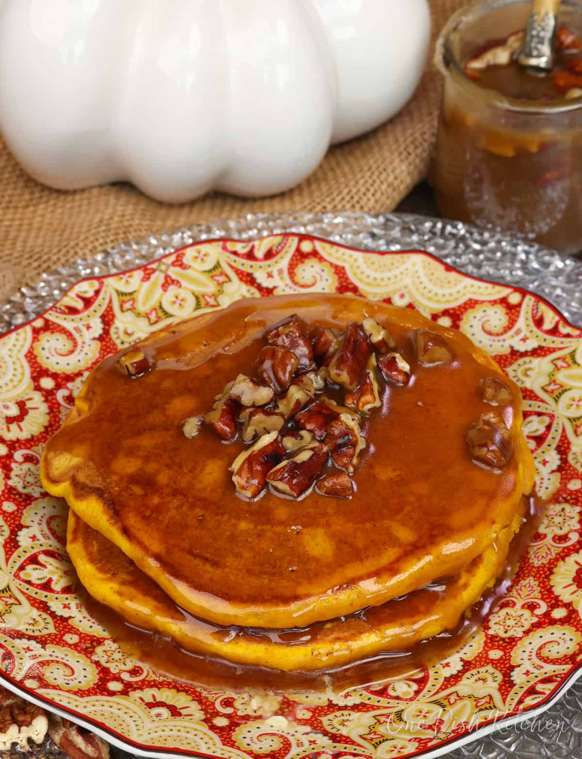 a stack of fluffy pumpkin pancakes with homemade butter pecan syrup poured over them.