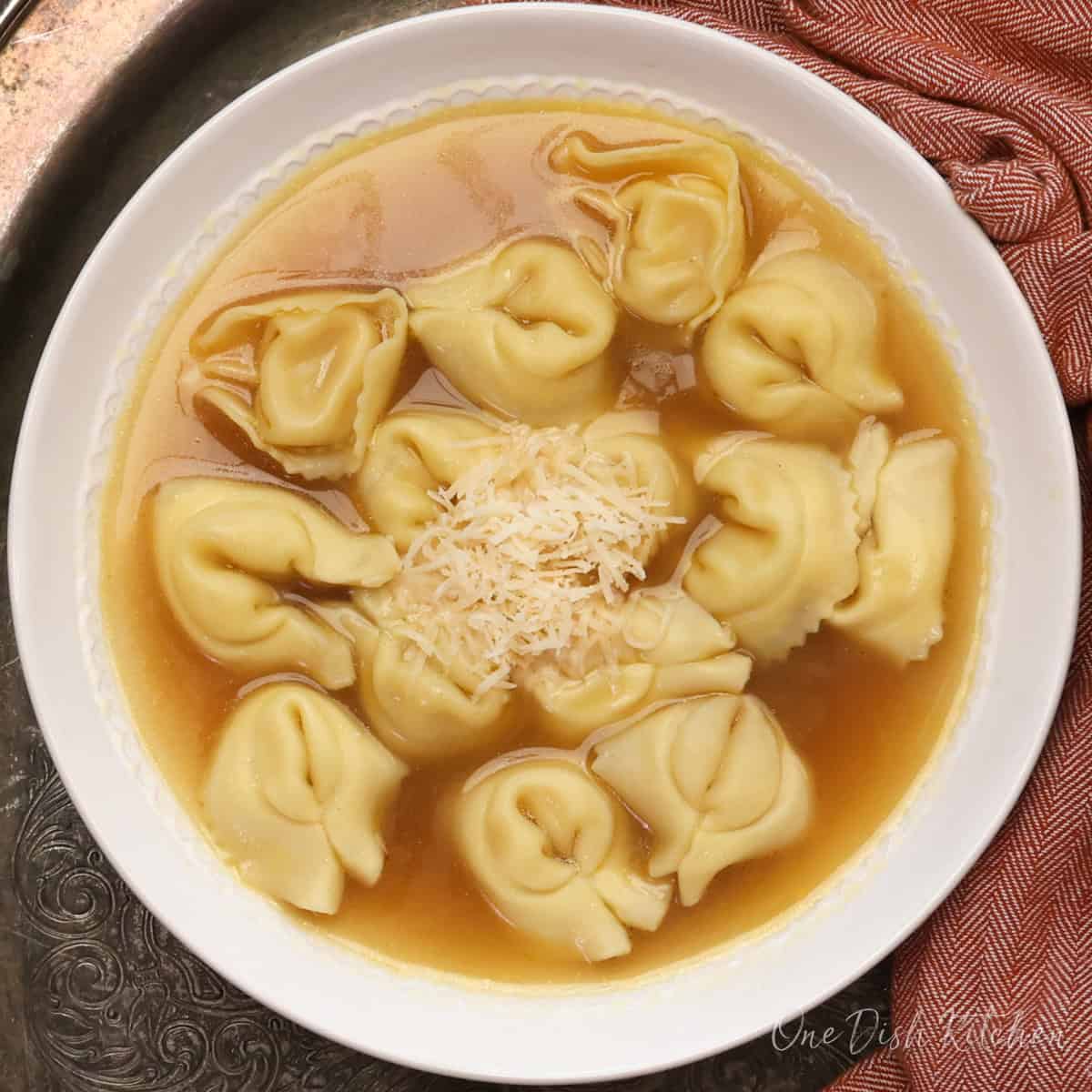 A bowl of Italian soup with cheese tortellini in golden broth topped with freshly grated Parmesan.