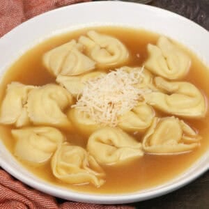 A bowl of tortellini en brodo with cheese tortellini in clear chicken broth topped with Parmesan cheese.
