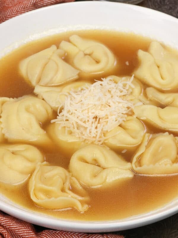 A bowl of tortellini en brodo with cheese tortellini in clear chicken broth topped with Parmesan cheese.