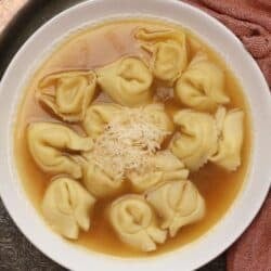 A bowl of tortellini en brodo with cheese tortellini in clear chicken broth topped with Parmesan cheese.