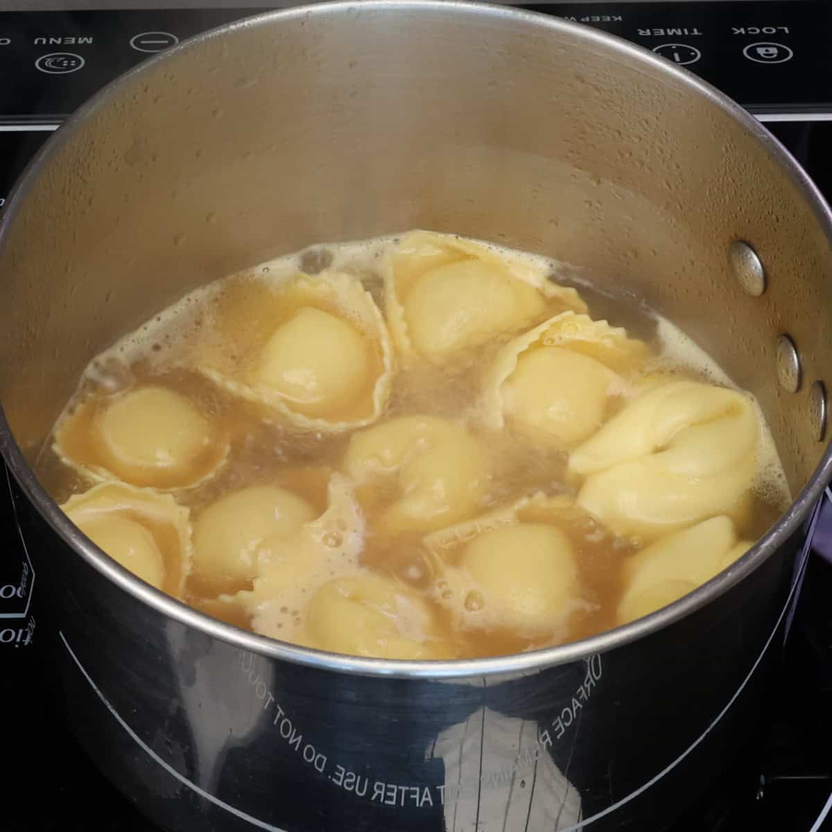 Cheese tortellini gently boiling in clear chicken broth as they float to the top when cooked.