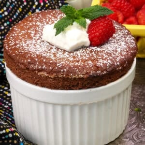 a chocolate souffle for one person in a white ramekin topped with whipped cream, a raspberry and fresh mint.