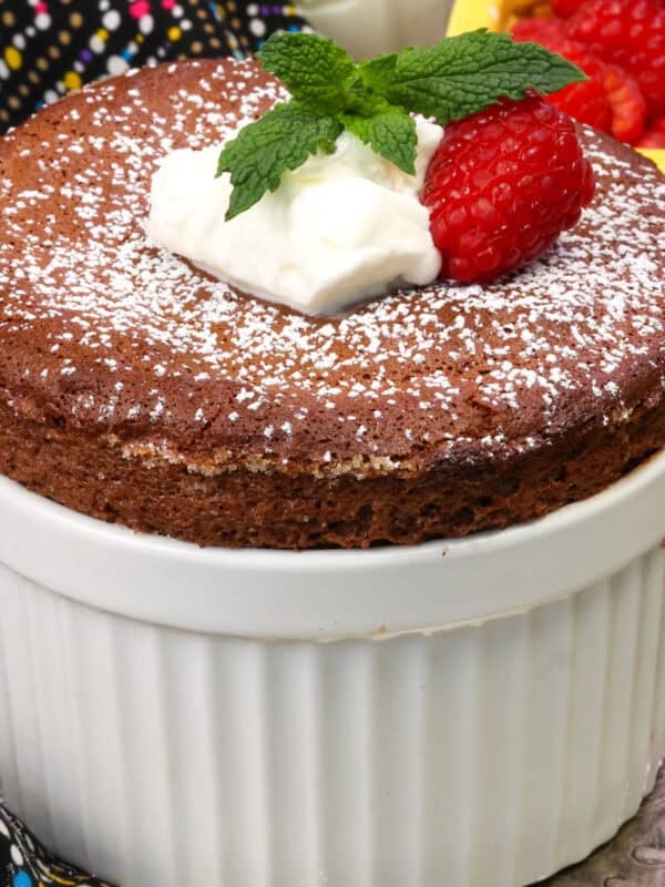 a chocolate souffle for one person in a white ramekin topped with whipped cream, a raspberry and fresh mint.