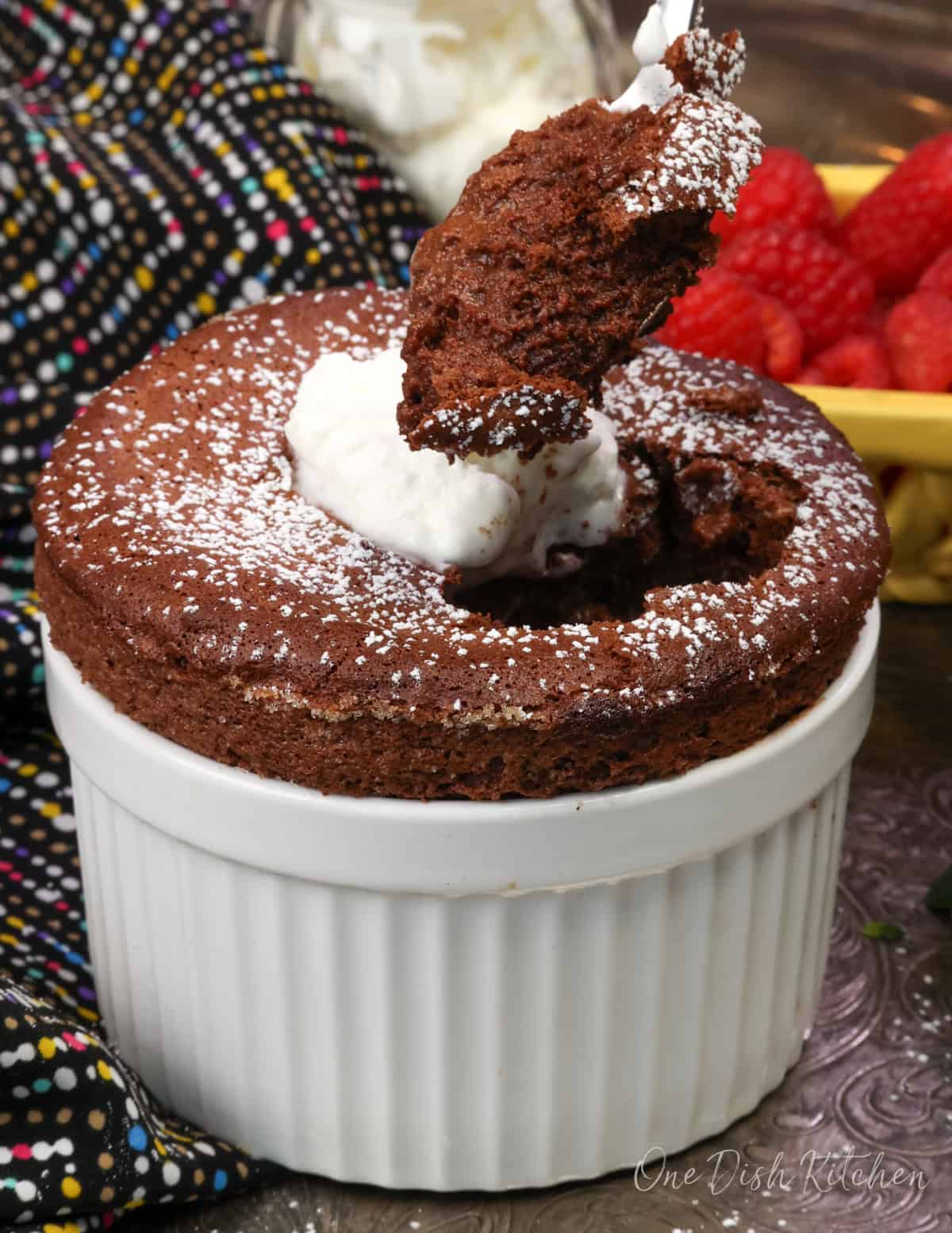 chocolate soufflé for one in a ramekin topped with powdered sugar and a spoon.