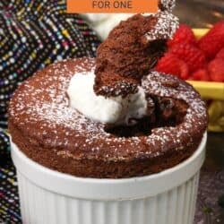a chocolate souffle for one person in a white ramekin topped with whipped cream, a raspberry and fresh mint.