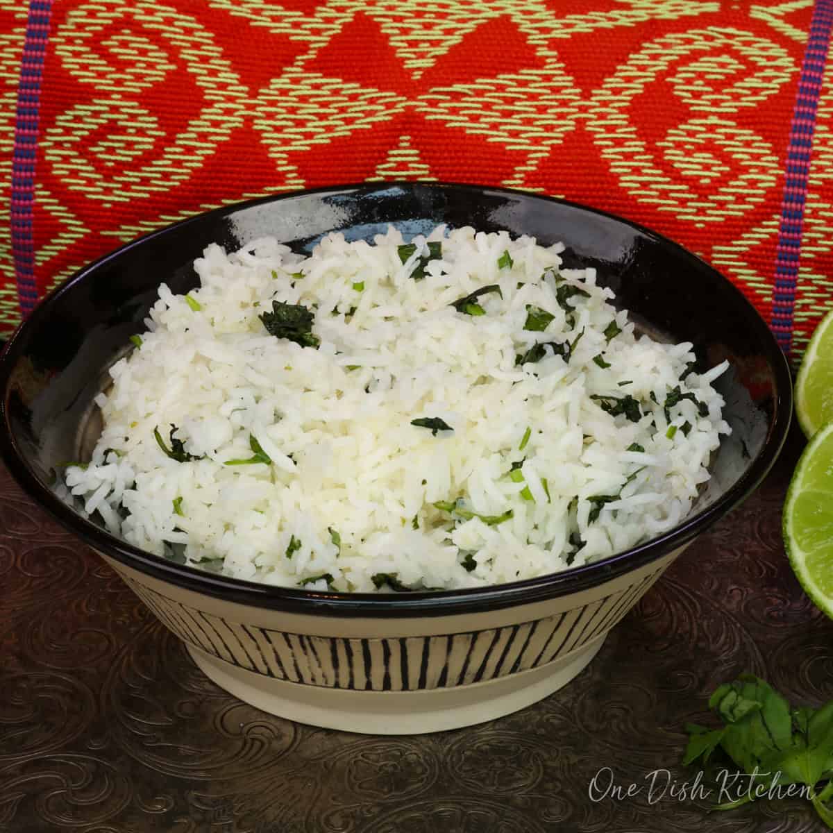a single serving of cilantro lime rice in a black bowl next to limes and fresh cilantro.