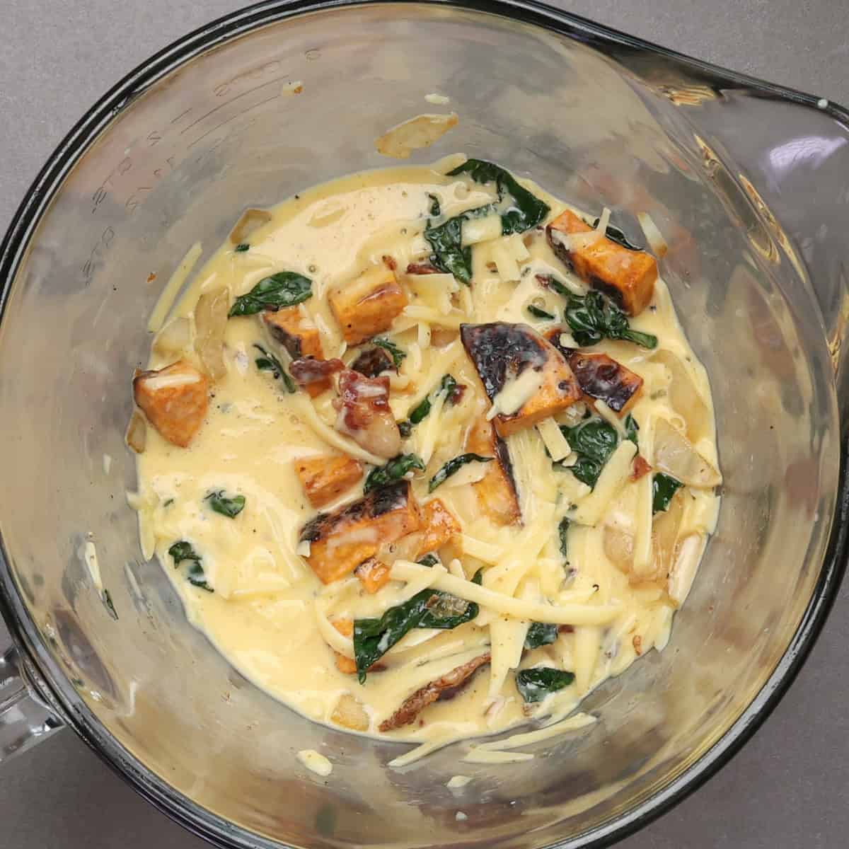 roasted sweet potatoes, kale, onions, eggs, cream and cheese in a mixing bowl.