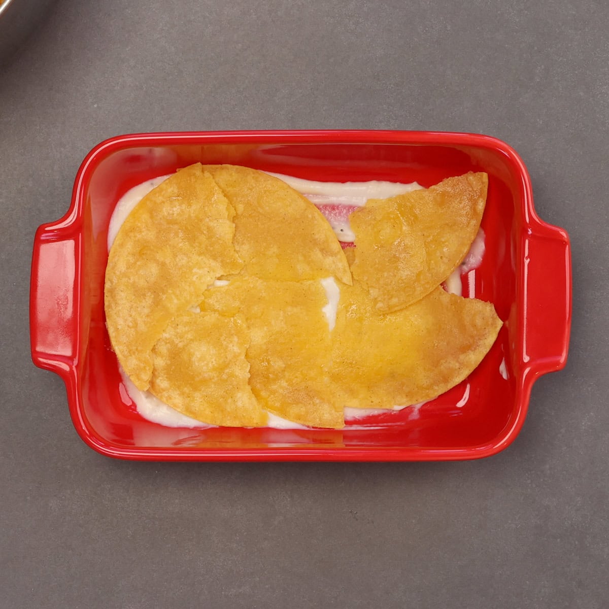 torn corn tortillas lining the bottom of a small baking dish.