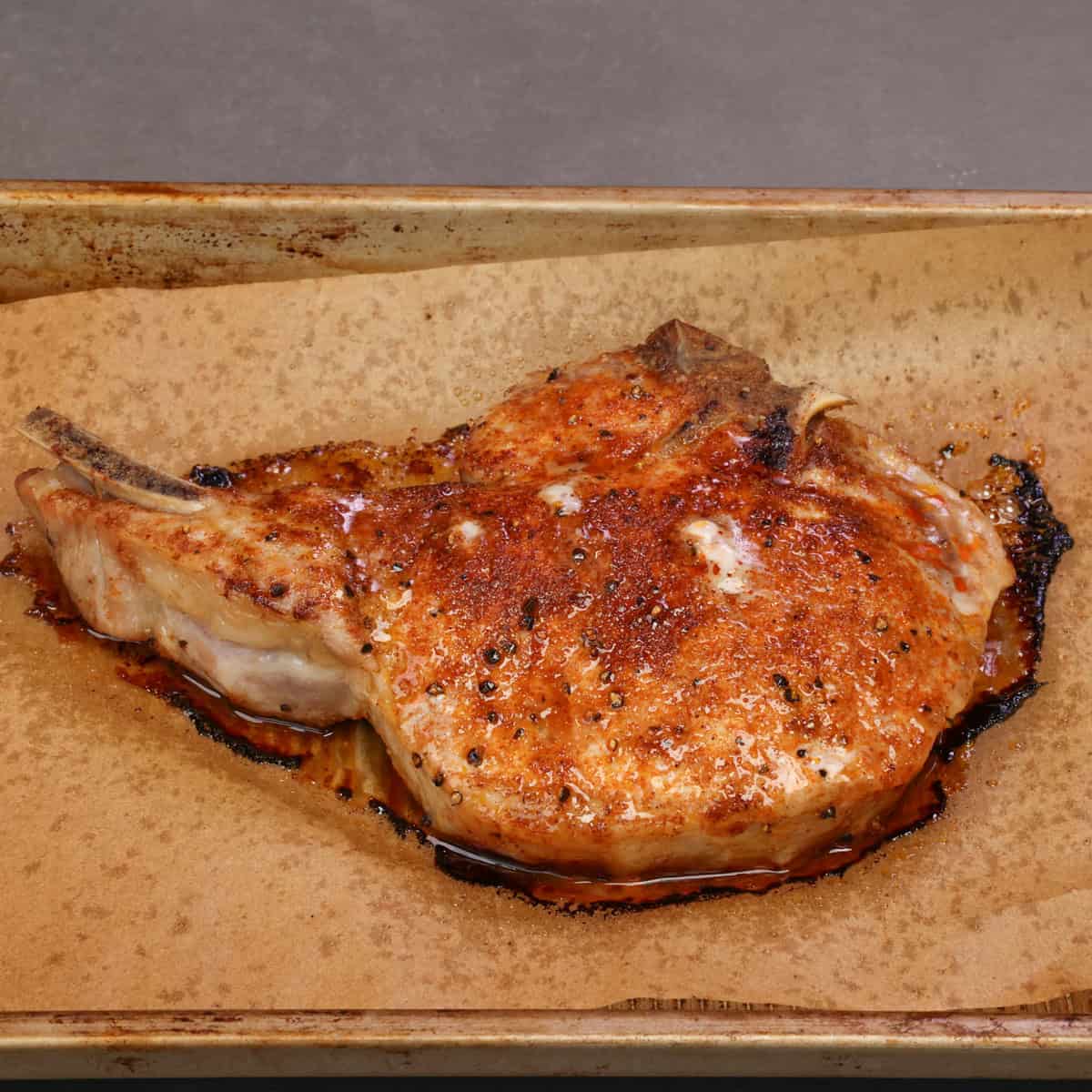 a single baked bone in pork chop seasoned and topped with butter, resting on a baking sheet.