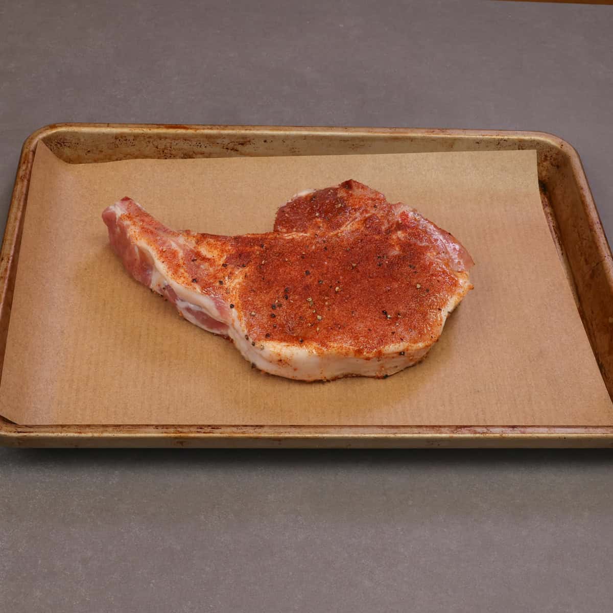 one seasoned unbaked bone in pork chop on a baking sheet.