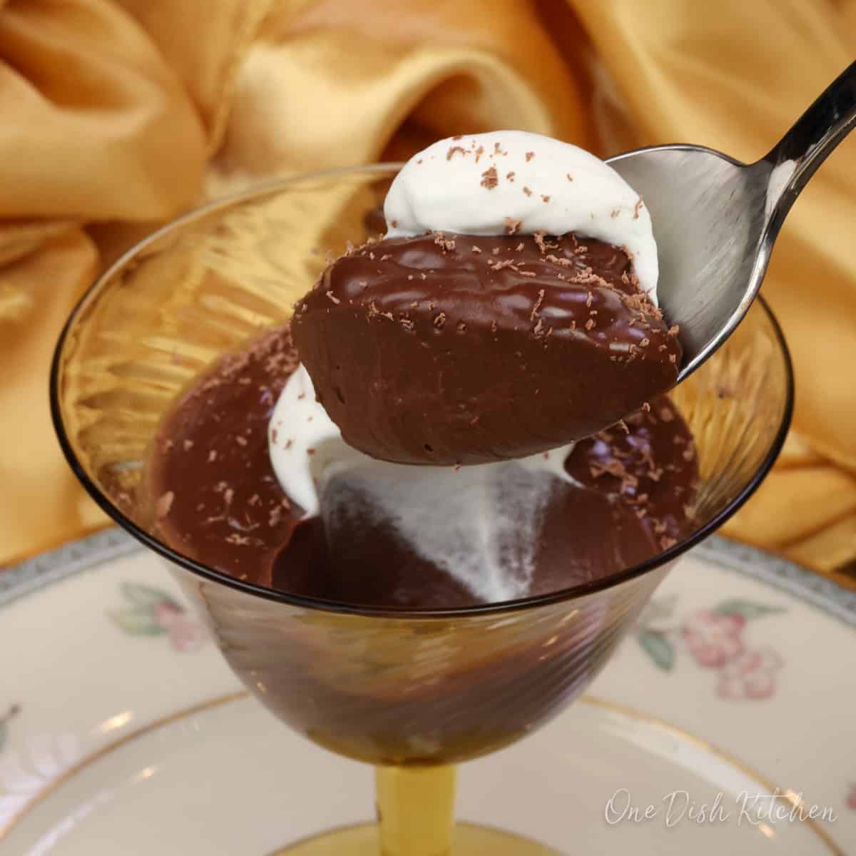 a chocolate pot de crème in a dessert dish with a spoon above the dish.