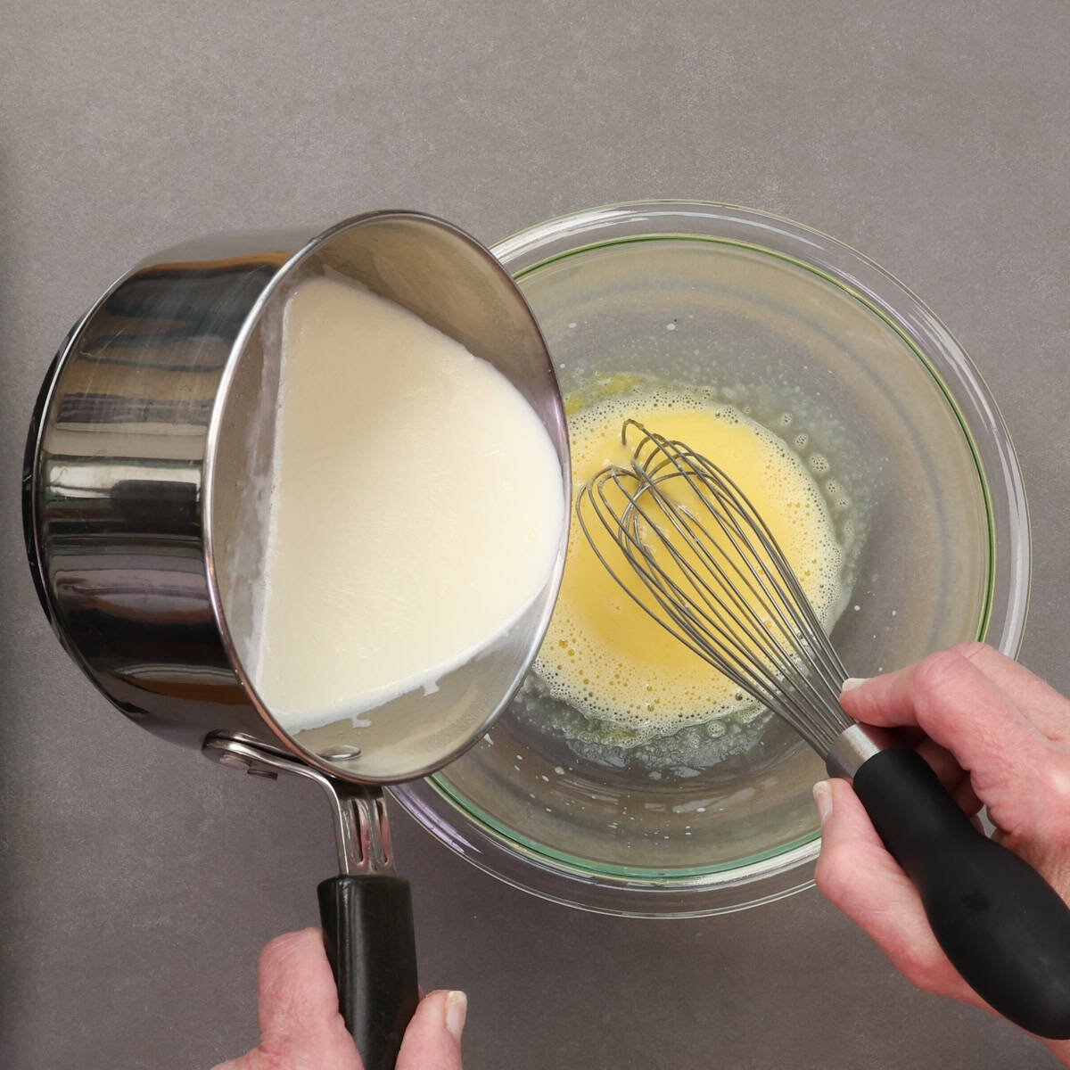 Whisking hot milk into egg yolk to temper the custard mixture.