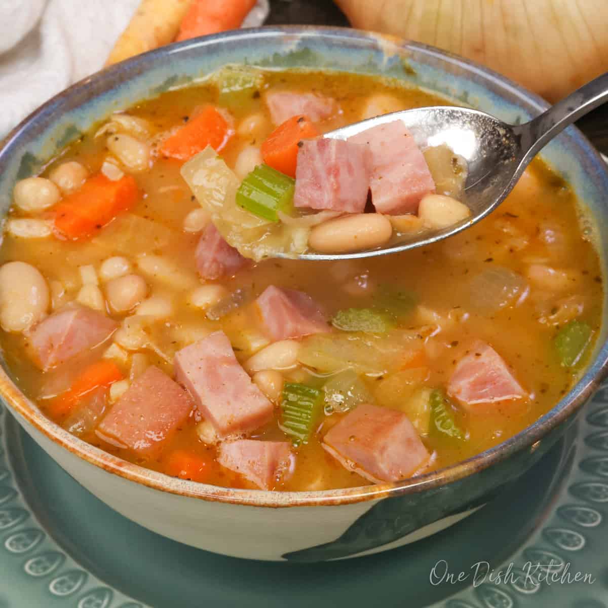 a single serving of ham and bean soup in a bowl with a spoon on the side.
