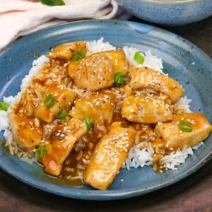 single serving orange chicken over white rice on a blue plate.