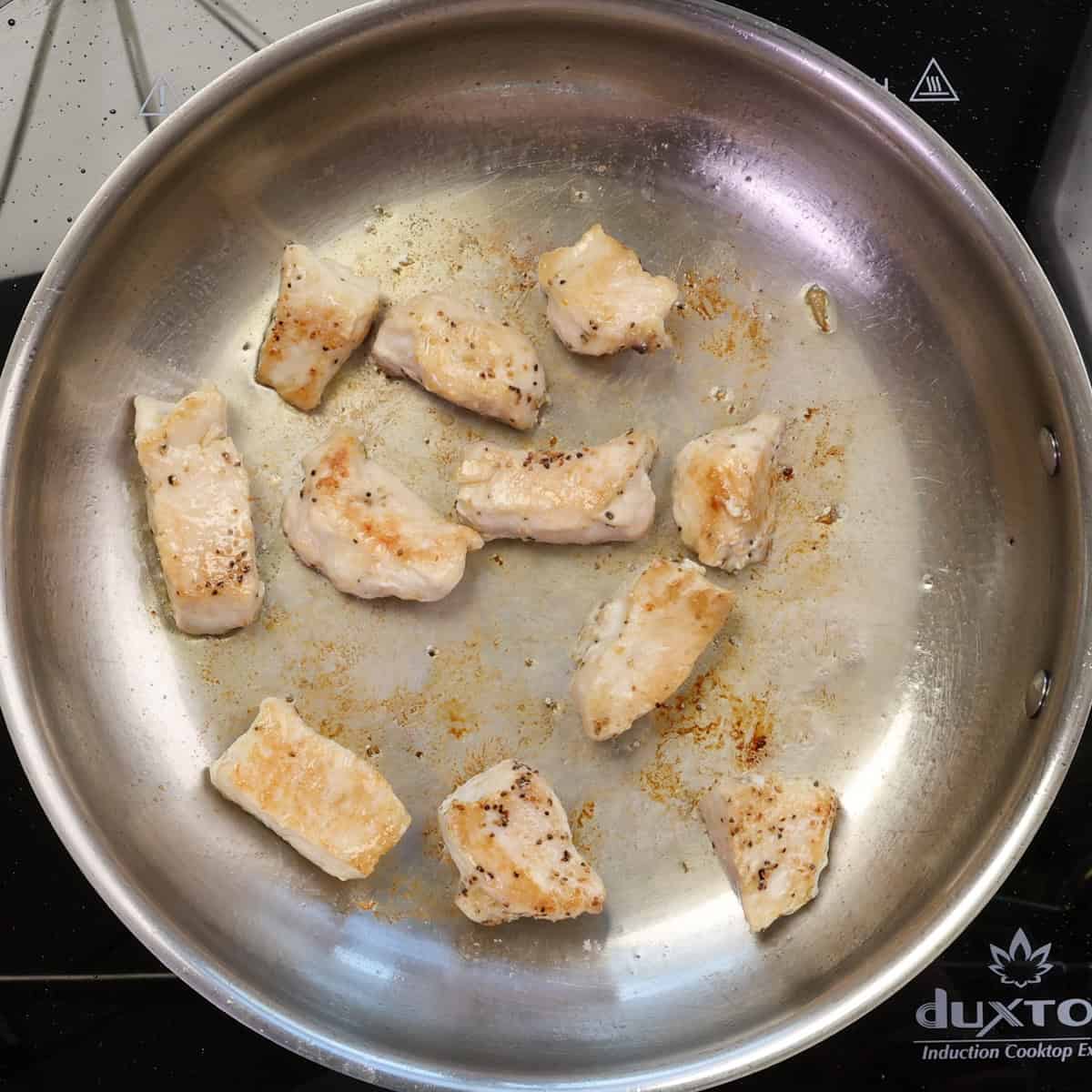 chicken pieces cooking in a skillet.