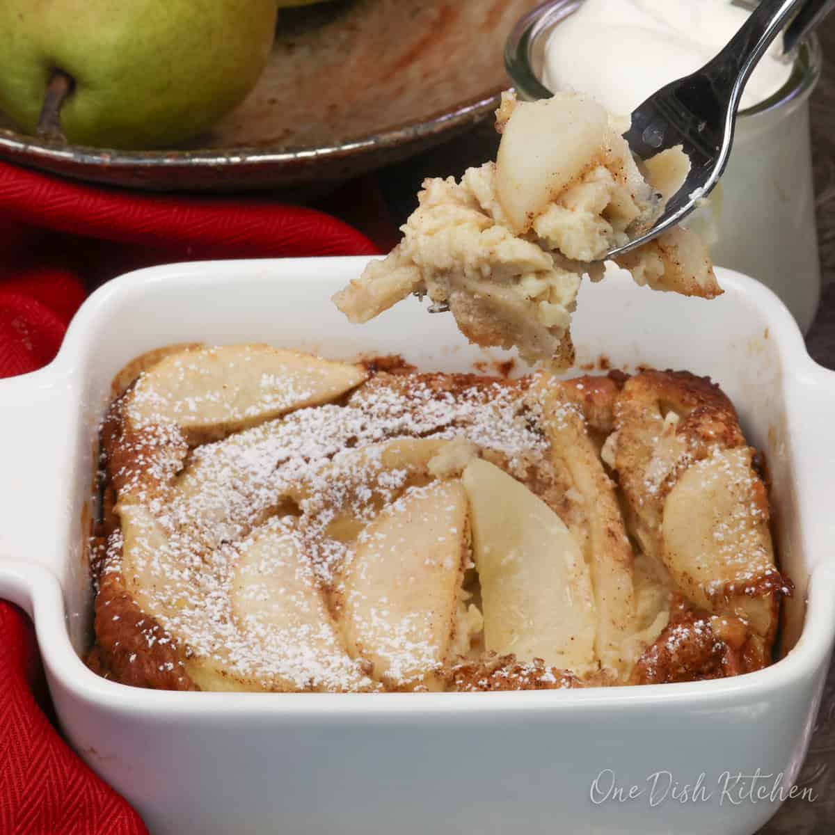 a small pear clafoutis in a square baking dish topped with powdered sugar.
