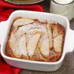 a single serving pear clafoutis in a small baking dish next to a bowl of pears.