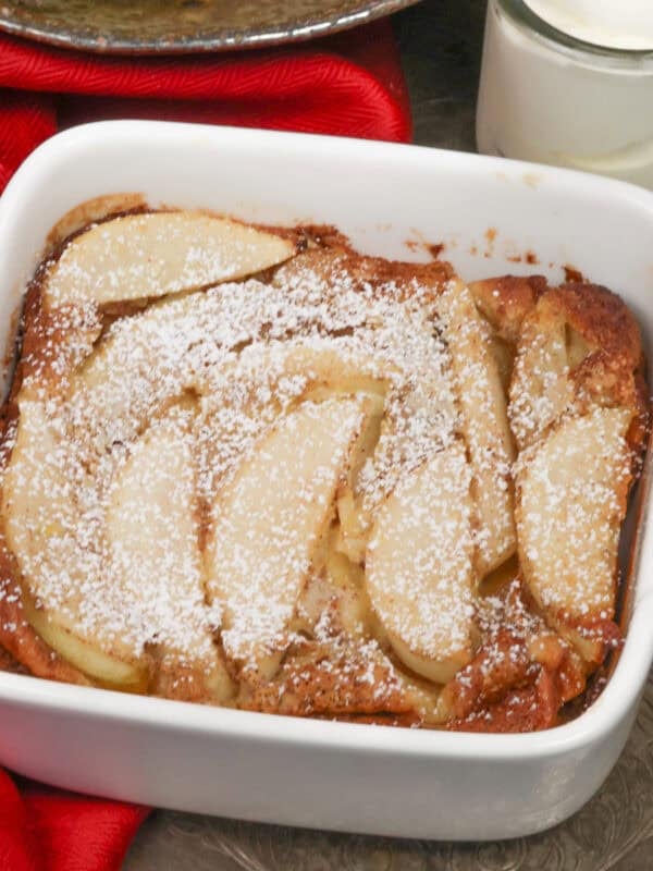 a single serving pear clafoutis in a small baking dish next to a bowl of pears.