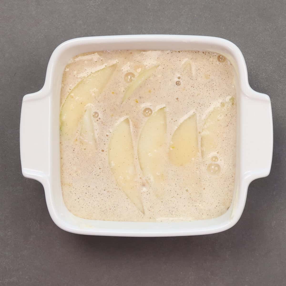 an unbaked pear clafoutis in a baking dish.