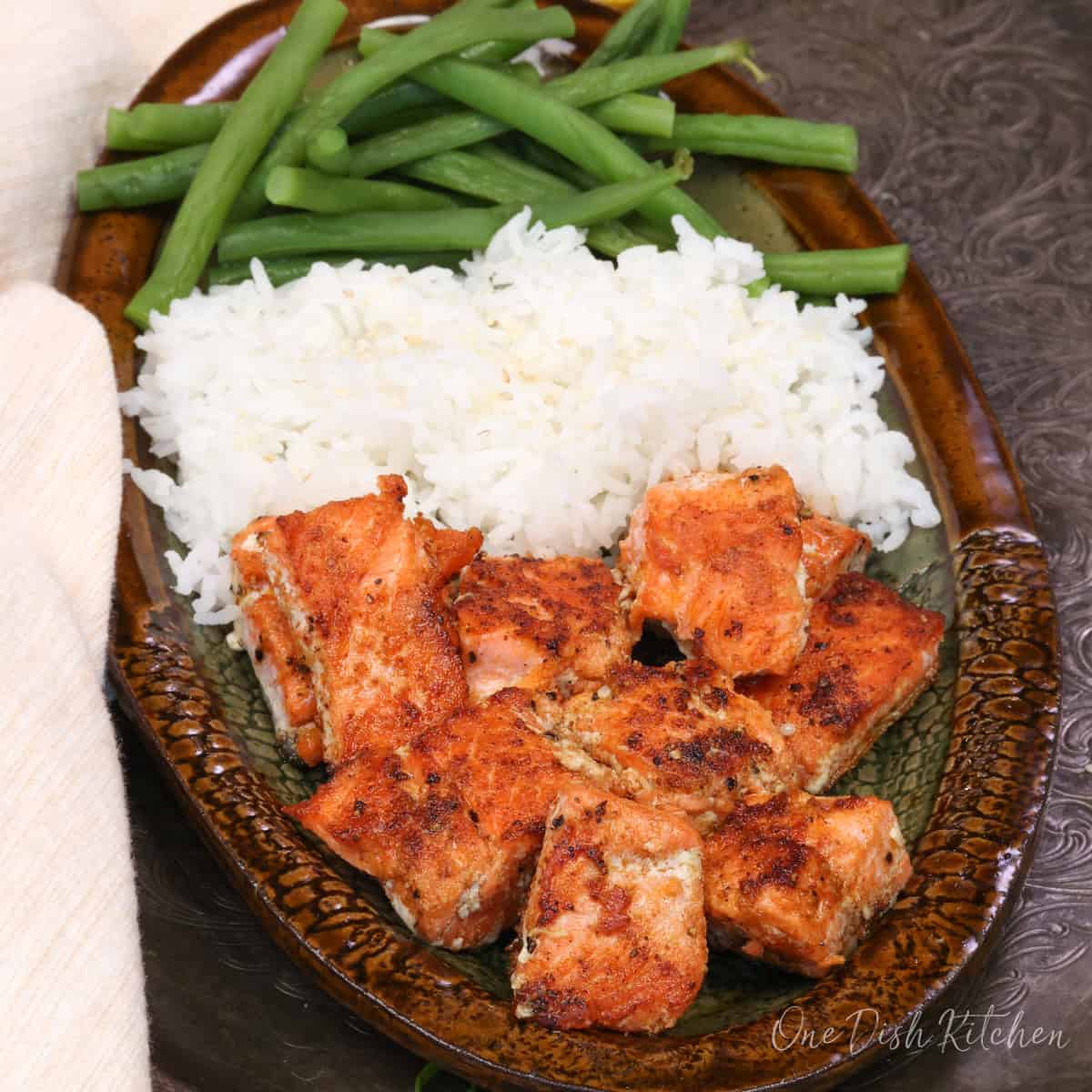a single serving of baked salmon bites on a plate with rice and green beans.