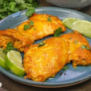 a single serving of tandoori chicken made with two boneless skinless chicken thighs on a blue plate.