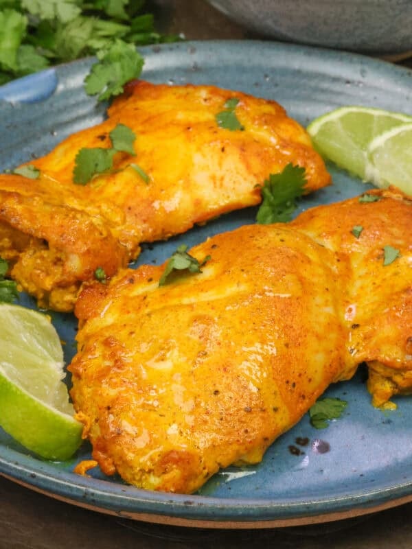 a single serving of tandoori chicken made with two boneless skinless chicken thighs on a blue plate.