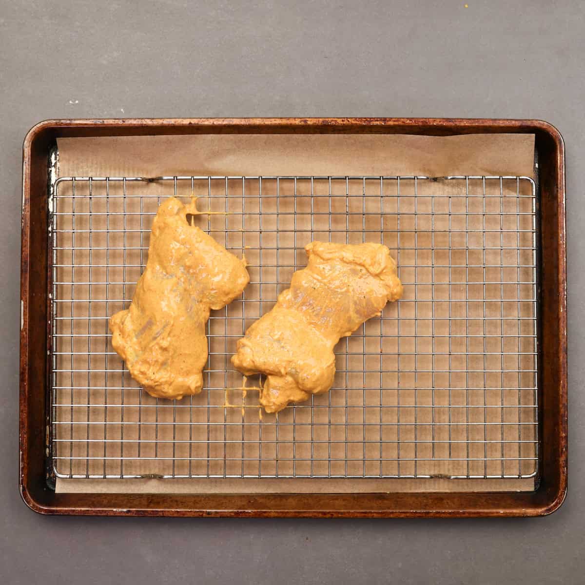 two chicken thighs coated with tandoori chicken marinade on a baking sheet.