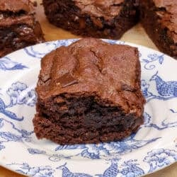 a single flourless brownie on a plate next to three flourless chocolate brownies and a red napkin.
