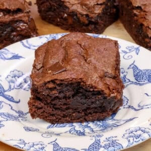 a single flourless brownie on a plate next to three flourless chocolate brownies and a red napkin.