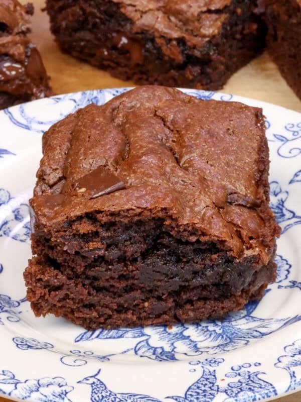 a single flourless brownie on a plate next to three flourless chocolate brownies and a red napkin.